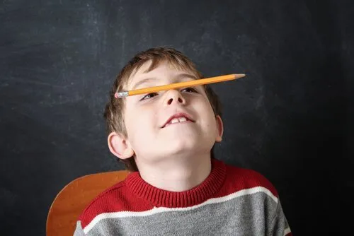 Chłopiec balansuje ołówkiem na nosie, zagubiony wzrokiem gdzieś w górze — klasyczny obraz trudności z koncentracją u dziecka z ADHD
