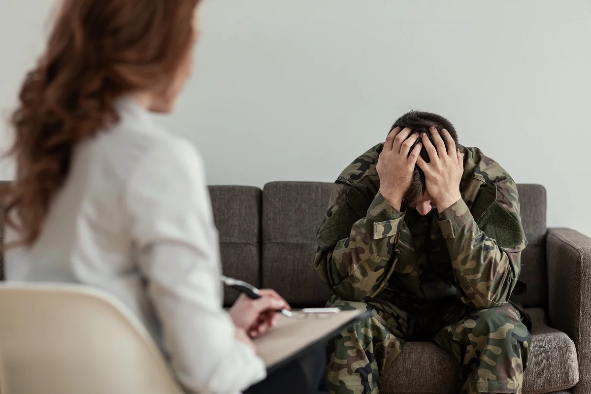 Żołnierz z głową w dłoniach podczas sesji terapeutycznej — PTSD po traumie bojowej, jeden z najbardziej rozpoznawalnych obrazów zaburzenia stresowego pourazowego